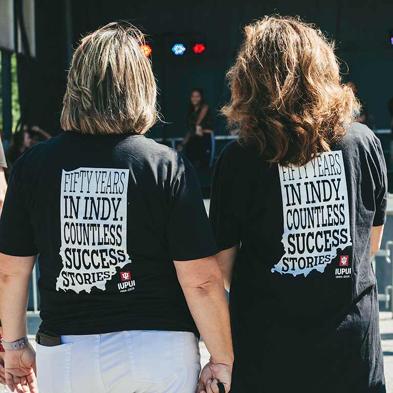 Two women stand in matching t-shirts that say 'Fifty years in Indy. Countless success stories.'