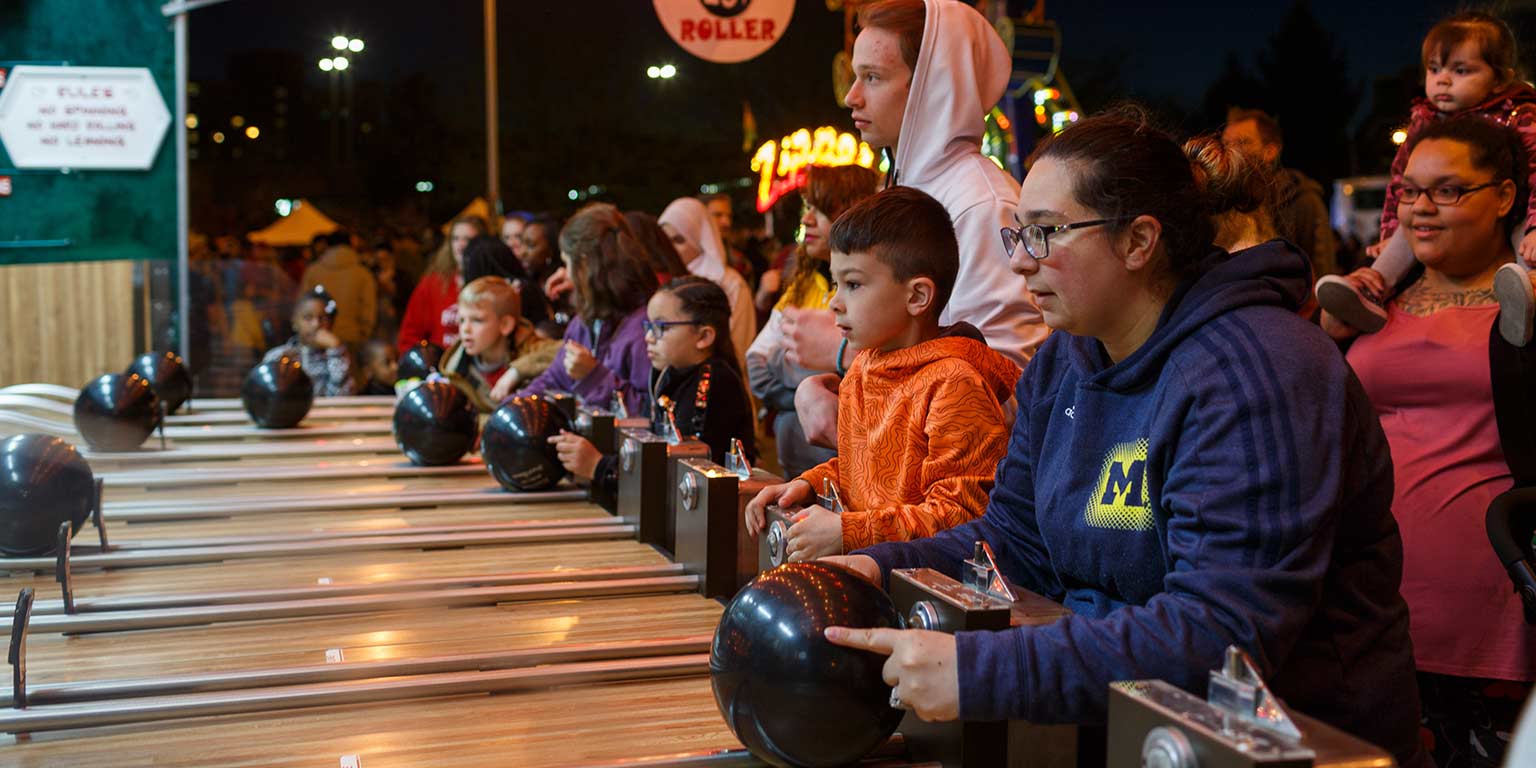 Students and children play a carnival game with bowling balls at Jagapalooza.