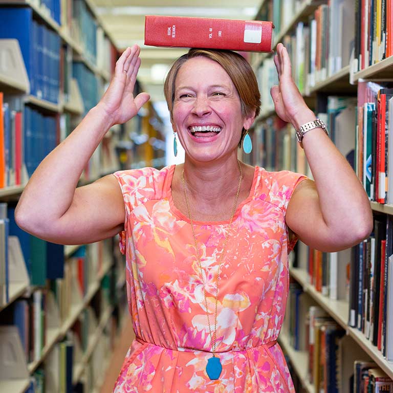 Kristi Palmer in the book stacks balancing a book on her head.