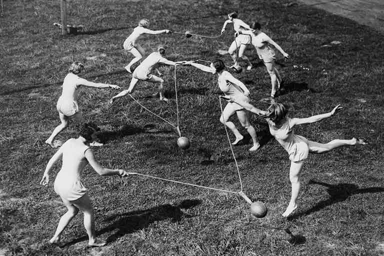 Female students at the Normal College swing medicine balls between two people with ropes. Black and white photo.